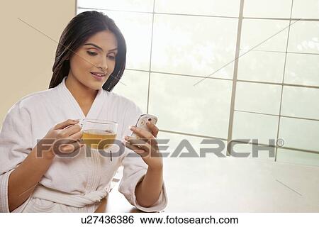 Young woman in bathrobe text messaging while holding tea cup at dining table View Large Photo Image Stock Photograph - Young woman in bathrobe text messaging while holding tea cup at dining table . Fotosearch