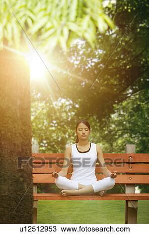 Stock Image - Young woman in lotus position meditating in a park . Fotosearch