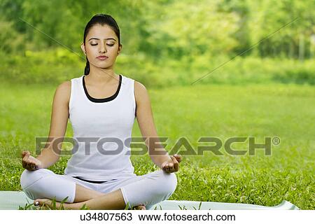 Young woman in lotus position meditating in a park View Large Photo Image Stock Image - Young woman in lotus position meditating in a park . Fotosearch