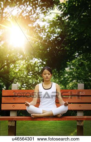 Stock Image - Young woman in lotus position meditating in a park . Fotosearch