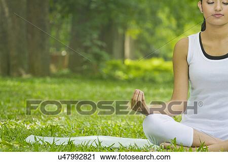 Stock Image - Young woman in lotus position meditating in a park . Fotosearch