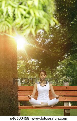 Young woman in lotus position meditating in a park View Large Photo Image Stock Photo - Young woman in lotus position meditating in a park . Fotosearch