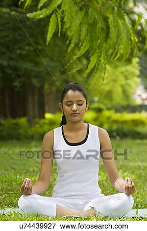 Young woman in lotus position meditating in a park View Large Photo Image Stock Photo - Young woman in lotus position meditating in a park . Fotosearch
