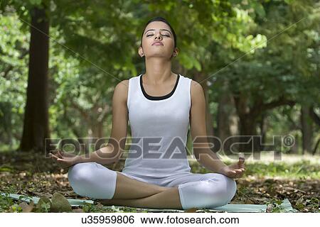 Stock Photograph - Young woman in lotus position meditating in a park . Fotosearch