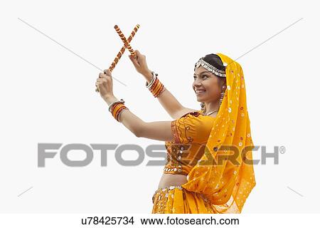 Picture - Young woman in traditional wear performing Dandiya Raas over white background. Fotosearch