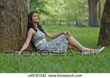 Stock Image - Young woman leaning against a tree . Fotosearch
