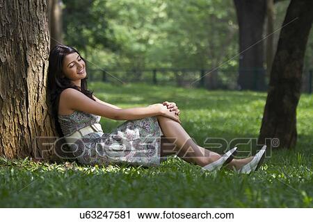 Stock Image - Young woman leaning against a tree . Fotosearch