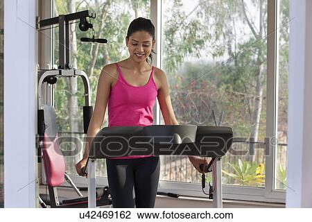 Young woman looking down while standing on treadmill View Large Photo Image Stock Image - Young woman looking down while standing on treadmill . Fotosearch