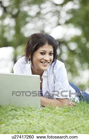Young woman lying on grass in lawn and using laptop View Large Photo Image Stock Image - Young woman lying on grass in lawn and using laptop . Fotosearch