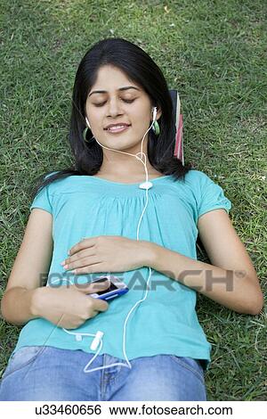 Young woman lying on grass listening to mp3 player View Large Photo Image Stock Photograph - Young woman lying on grass listening to mp3 player . Fotosearch