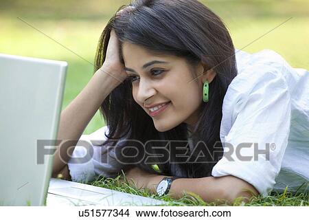 Picture - Young woman lying on grass using laptop . Fotosearch