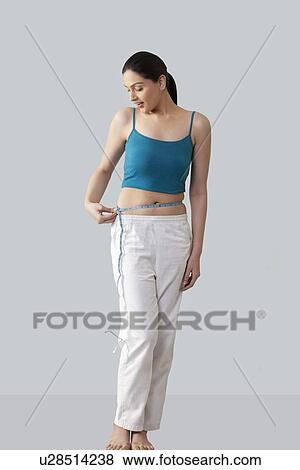Stock Photo - Young woman measuring waist isolated over gray background . Fotosearch