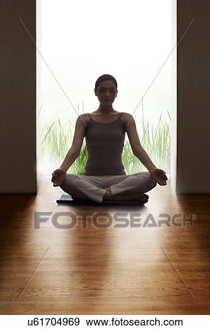 Stock Photo - Young woman meditating on hardwood floor. Fotosearch