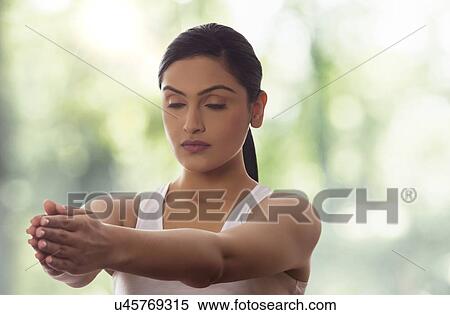 Stock Photography - Young woman meditating with arms out against glass window. Fotosearch