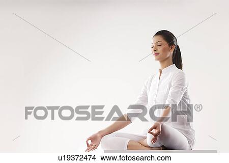 Picture - Young woman sitting in lotus position over white background . Fotosearch