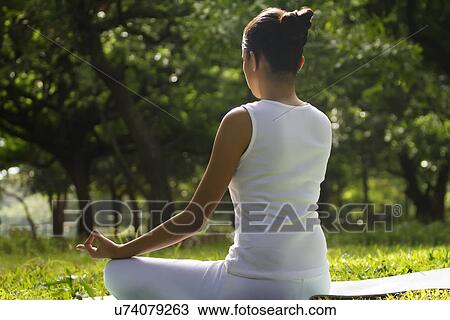 Stock Image - Young woman sitting in lotus position in a park . Fotosearch