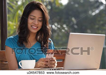 Stock Image - Young woman smiling while using cell phone . Fotosearch