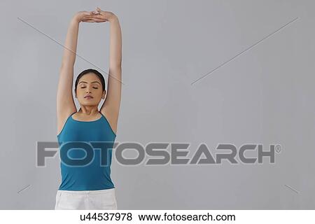 Young woman stretching arms upwards against gray background View Large Photo Image Stock Photo - Young woman stretching arms upwards against gray background. Fotosearch