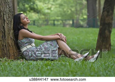 Stock Photo - Young woman thinking while leaning against a tree . Fotosearch