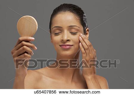 Stock Photograph - Young woman with eyes closed holding hand mirror . Fotosearch