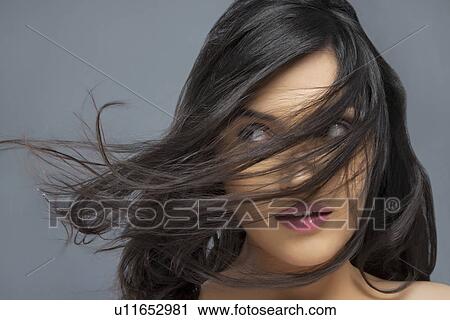 Young woman with hair blowing over face against colored background View Large Photo Image Stock Image - Young woman with hair blowing over face against colored background . Fotosearch