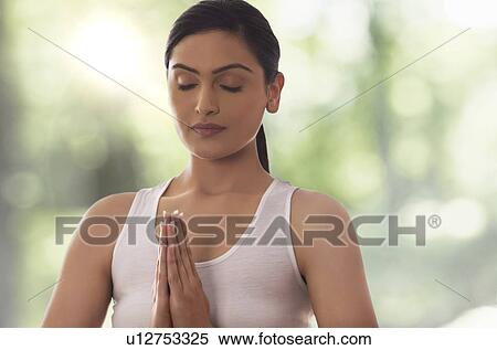 Stock Photography - Young woman with hands clasped meditating against glass window. Fotosearch