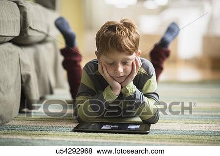 Stock Photo - Boy (6-7) lying on carpet and using tablet pc. Fotosearch