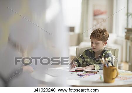 Stock Image - Boy (6-7) sitting and drawing in family room . Fotosearch