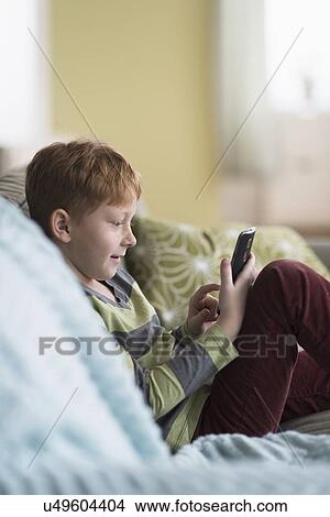 Boy (6-7) sitting on couch and using cell phone View Large Photo Image Picture - Boy (6-7) sitting on couch and using cell phone. Fotosearch