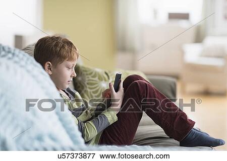 Stock Photo - Boy (6-7) sitting on couch and using cell phone. Fotosearch
