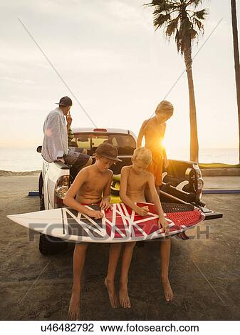 Boys (6-7, 10-11, 14-15) waxing surfboard at sunset View Large Photo Image Stock Image - Boys (6-7, 10-11, 14-15) waxing surfboard at sunset. Fotosearch