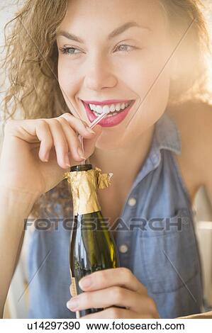 Stock Image - Cheerful young woman sipping champagne from bottle. Fotosearch