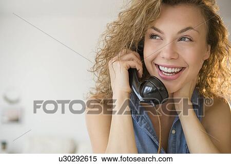 Stock Photography - Cheerful young woman talking on landline phone. Fotosearch