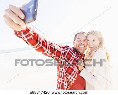 Stock Photograph - Couple taking selfie on beach. Fotosearch