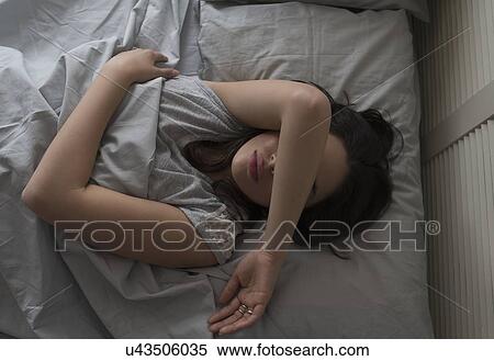 Stock Photography - Elevated view of young woman sleeping in bed. Fotosearch