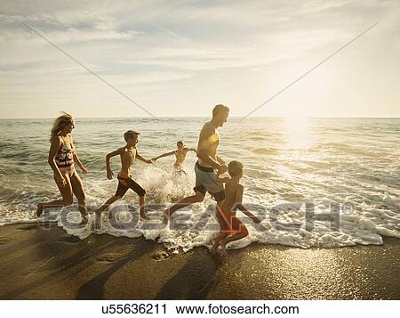 Stock Image - Family with three children (6-7, 10-11, 14-15) running on beach. Fotosearch