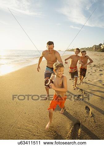 Father playing football on beach with his three sons (6-7, 10-11, 14-15) View Large Photo Image Stock Image - Father playing football on beach with his three sons (6-7, 10-11, 14-15). Fotosearch
