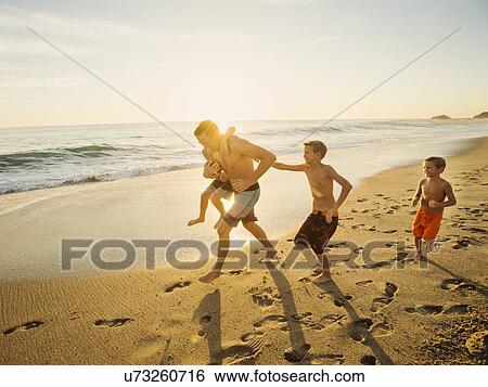 Father playing football on beach with his three sons (6-7, 10-11, 14-15) View Large Photo Image Stock Photograph - Father playing football on beach with his three sons (6-7, 10-11, 14-15). Fotosearch