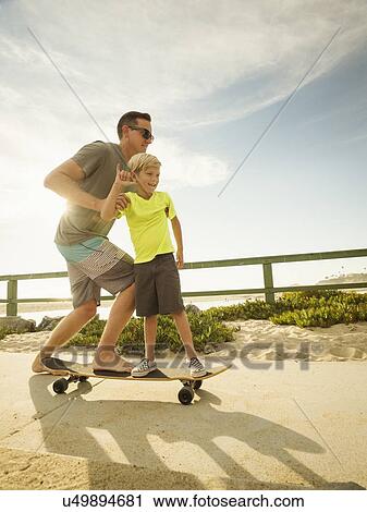 Stock Image - Father skateboarding with his son (6-7). Fotosearch