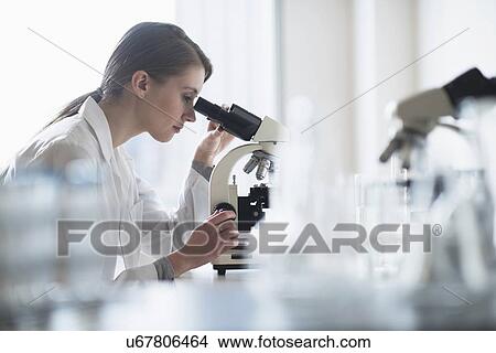 Picture - Female lab technician analyzing sample through microscope. Fotosearch