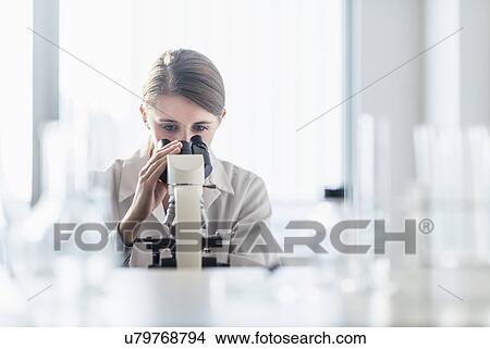 Picture - Female lab technician analyzing sample through microscope. Fotosearch