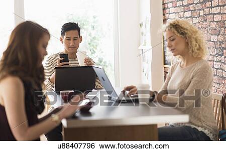 Stock Photograph - Friends sitting in cafe, using laptops and digital tablet. Fotosearch