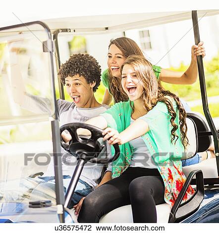 Stock Image - Group of friends (14-15) driving golf cart. Fotosearch