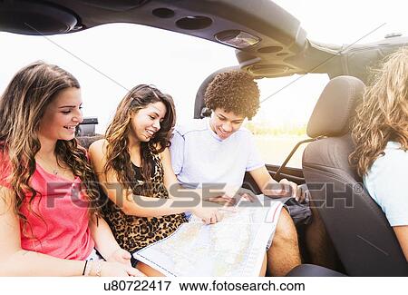 Stock Photo - Group of friends (14-15) reading map during road trip. Fotosearch