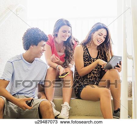 Group of friends (14-15) sitting on steps and using digital tablet and cell phones View Large Photo Image Stock Image - Group of friends (14-15) sitting on steps and using digital tablet and cell phones. Fotosearch