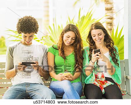 Group of friends (14-15) sitting on bench and texting View Large Photo Image Stock Image - Group of friends (14-15) sitting on bench and texting. Fotosearch