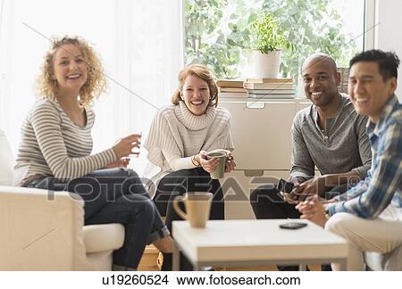 Group of friends hanging out in living room View Large Photo Image Picture - Group of friends hanging out in living room. Fotosearch