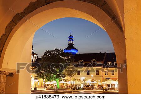 Stock Photo - Illuminated Main Square with sidewalk cafe and blue onion dome seen through arch. Fotosearch