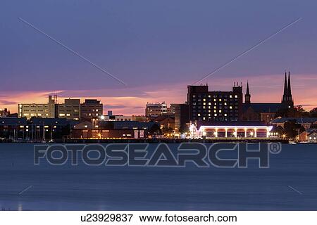 Stock Photo - Illuminated waterfront skyline against moody sky. Fotosearch