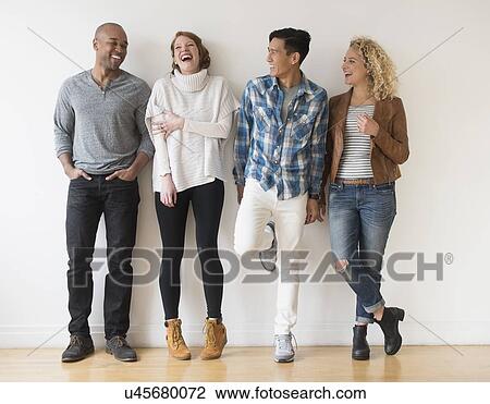 Stock Image - Laughing friends standing against white wall. Fotosearch